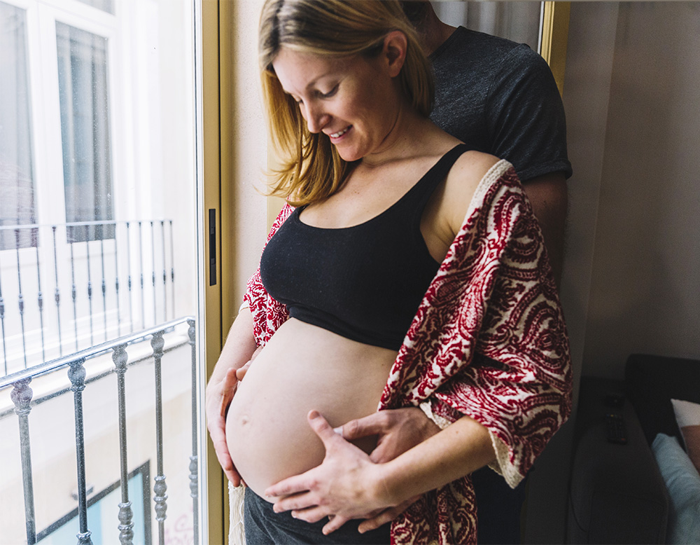 Femme enceinte entouré des bras de son conjoint, qui souhaitent offrir à leur bébé un départ serein avec la méthode Raconte-moi mon histoire